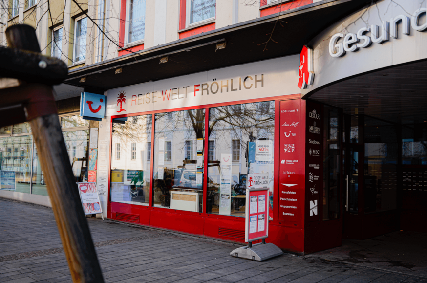Außenansicht der Reisebüro-Filiale „Reisewelt Fröhlich“ mit roter Markise.